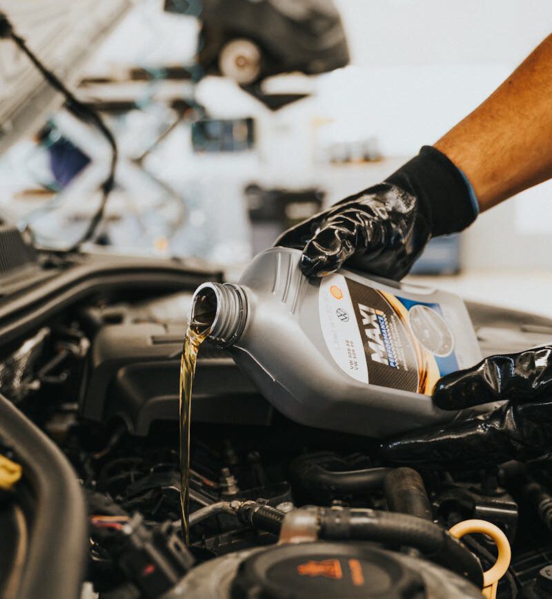 Ein Mechaniker lässt altes Motoröl aus einem Auto in eine Auffangwanne ab und bereitet den Einbau eines neuen Ölfilters vor. Symbol für den typischen Ablauf eines Ölwechsels.